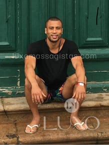Massagista de Luxo Mark sentado em uma escada e apoiado numa porta verde. Luxo Massagstas